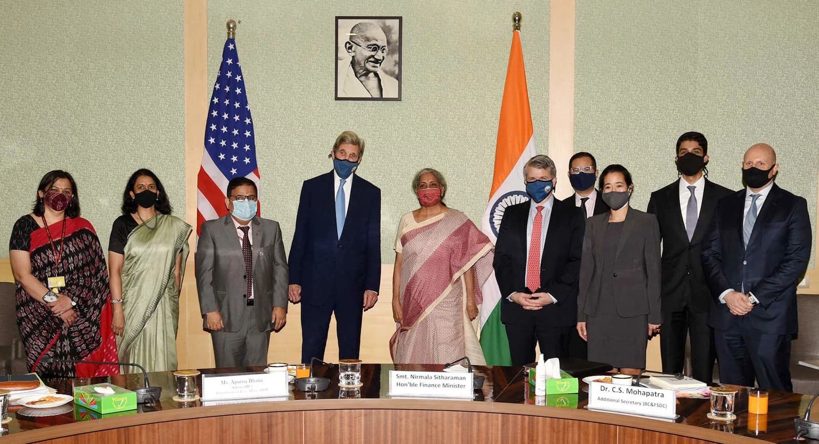 Nirmala Sitharaman, India's Finance Minister, standing with John Kerry and other delegates in a meeting room.