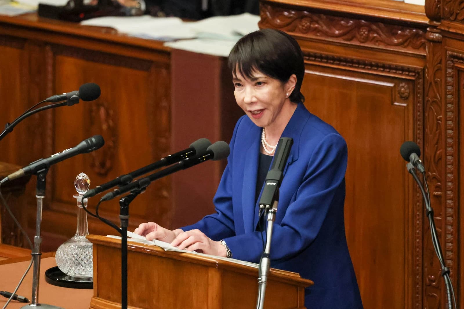 Prime Minister Takaichi speaks at a podium with microphones in the National Diet.