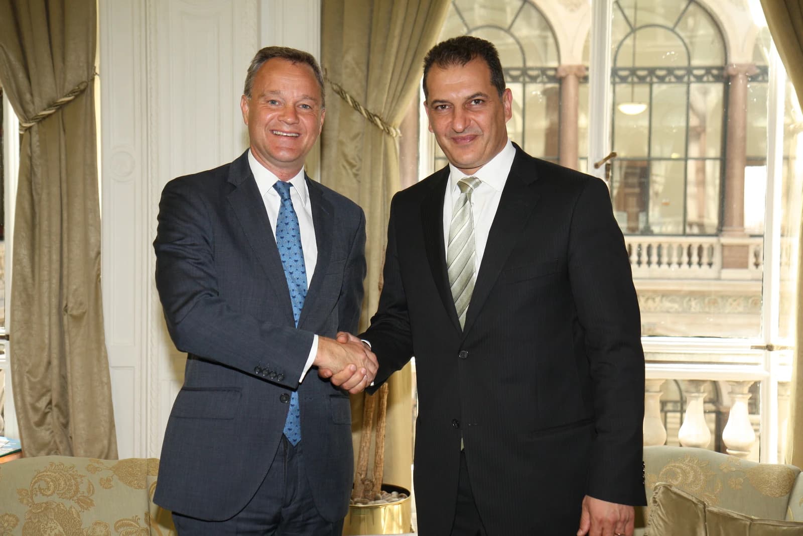 Yiorgos Lakkotrypis, Cypriot Minister for Energy, Commerce, Industry and Tourism, shaking hands with another man indoors.