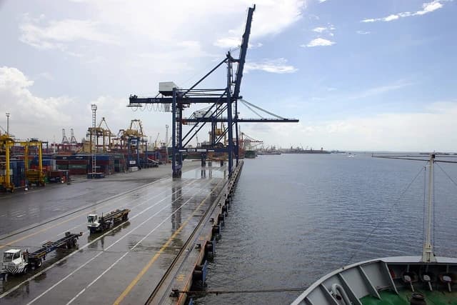 Tanjung Priok container terminal showing large cranes, stacked containers, and harbor.