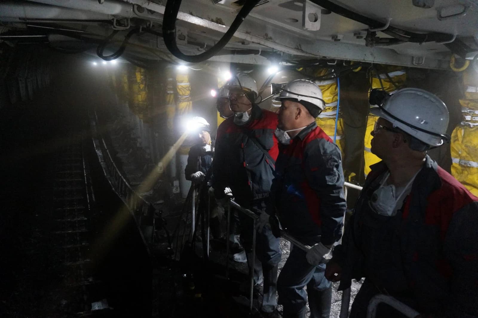 Coal miners in headlamps and protective gear working inside a mine.