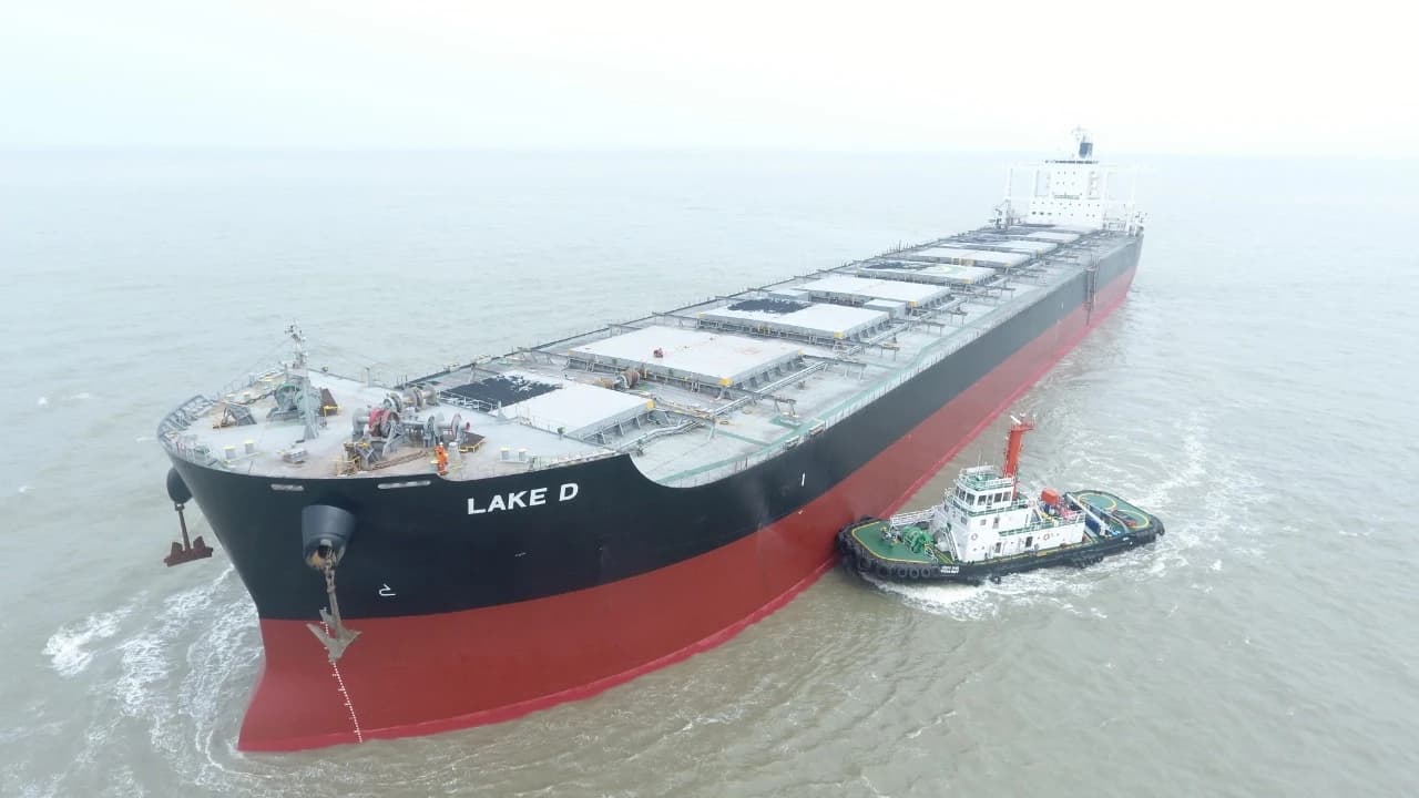 Cape-size bulk carrier M.V. Lake D being assisted by a tugboat in open water.