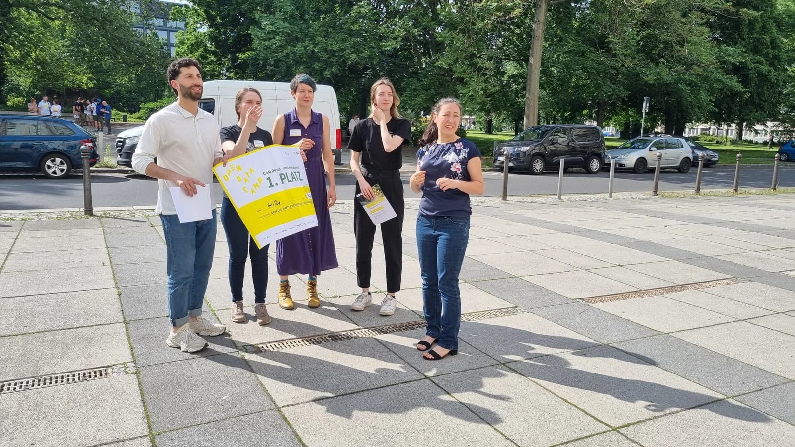 Five individuals stand outdoors, one holding a yellow sign that says 'Open Data Camp 1. Platz'.
