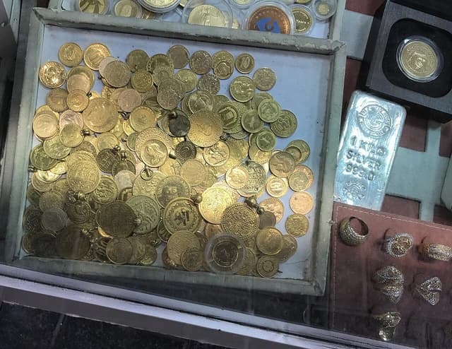 Gold coins, a silver bar, and rings are displayed in a shop window.