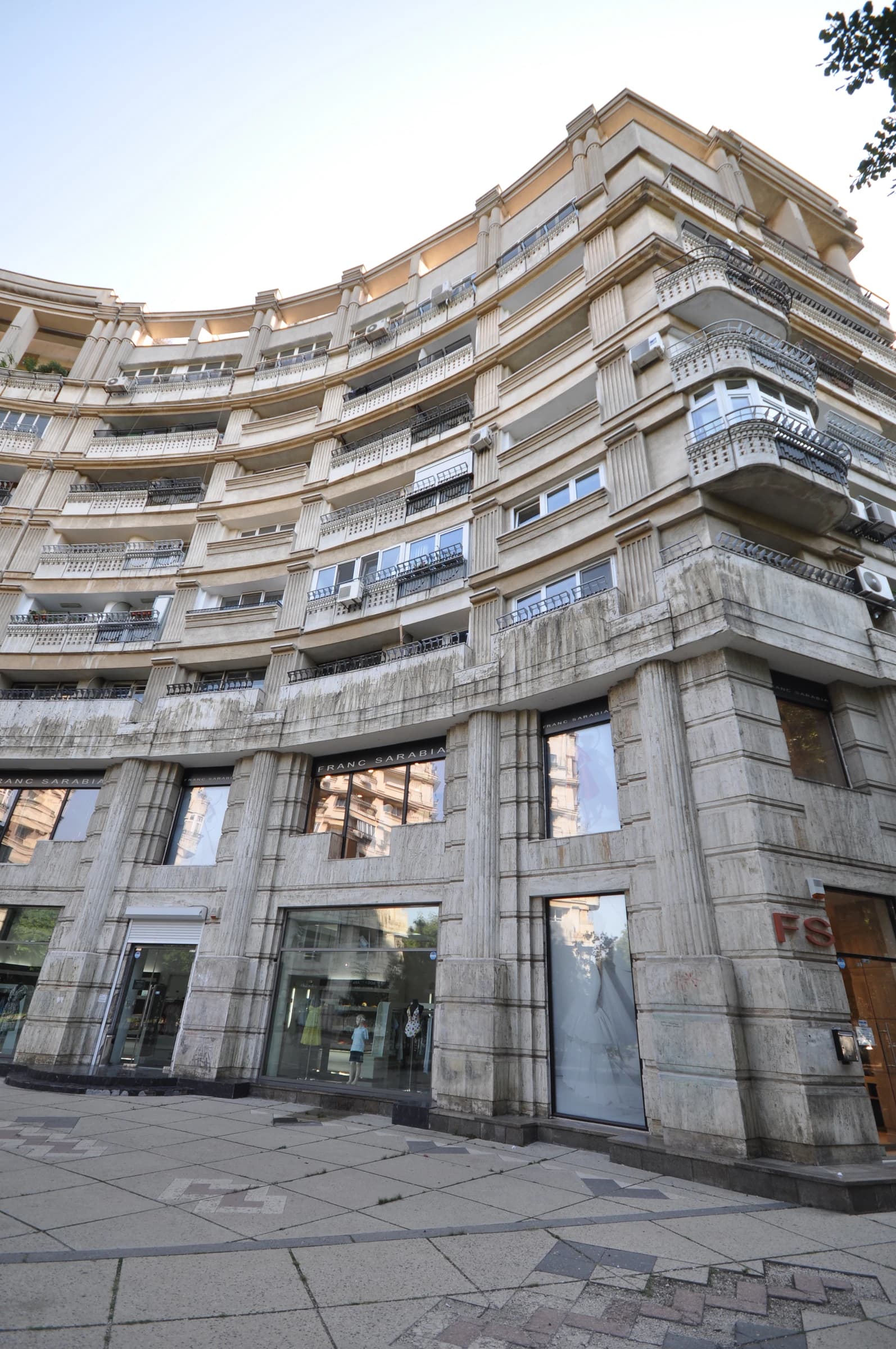 Curved facade of an ornate apartment building with shops on the ground floor.