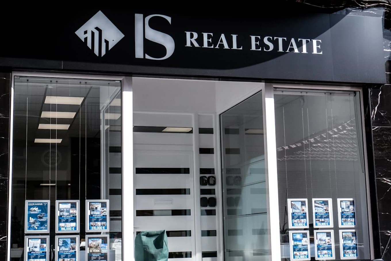 Exterior of 'IS Real Estate' office with property listings displayed in the window.