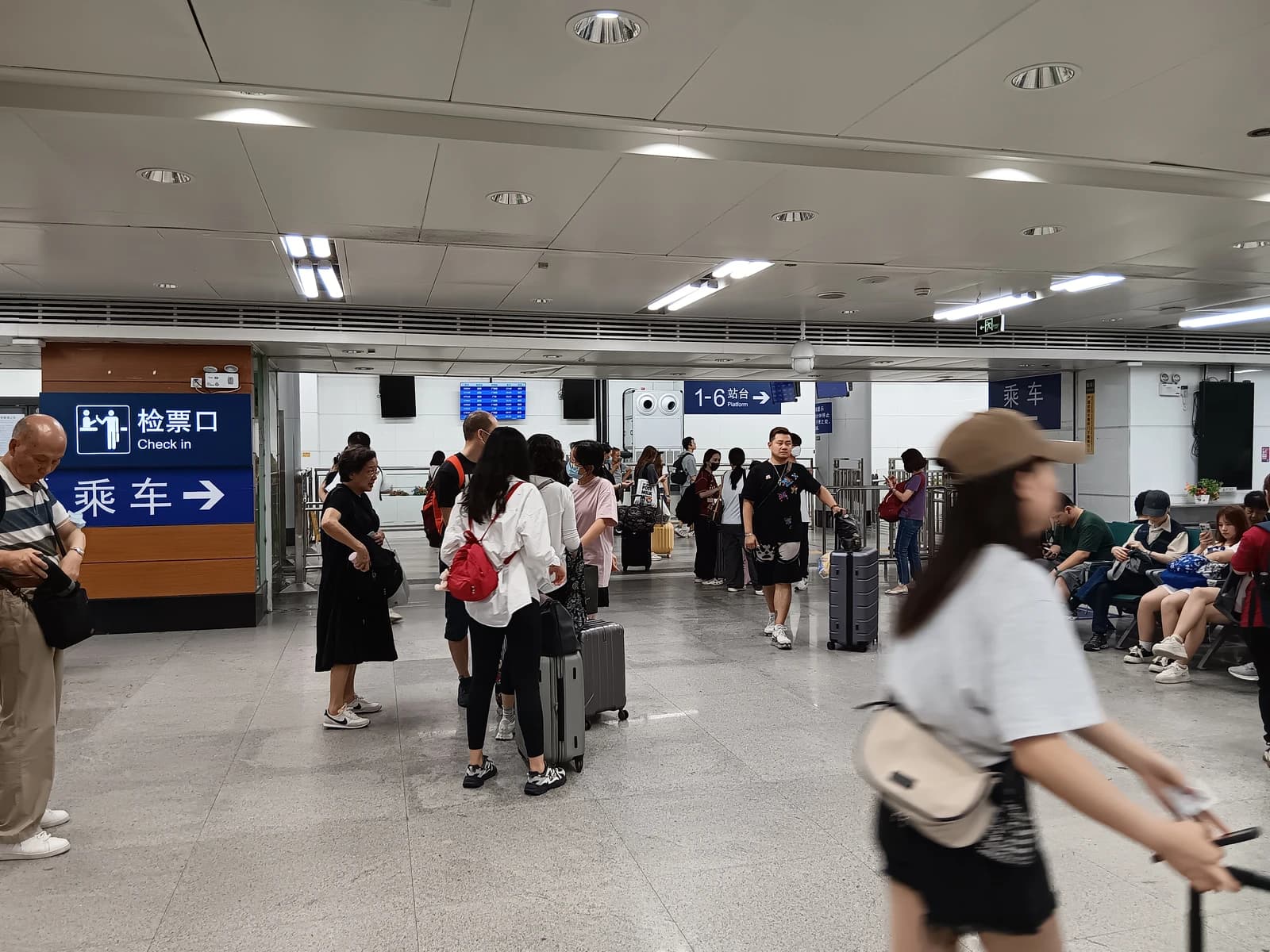 Travelers wait with luggage in a brightly lit train station waiting room in China.