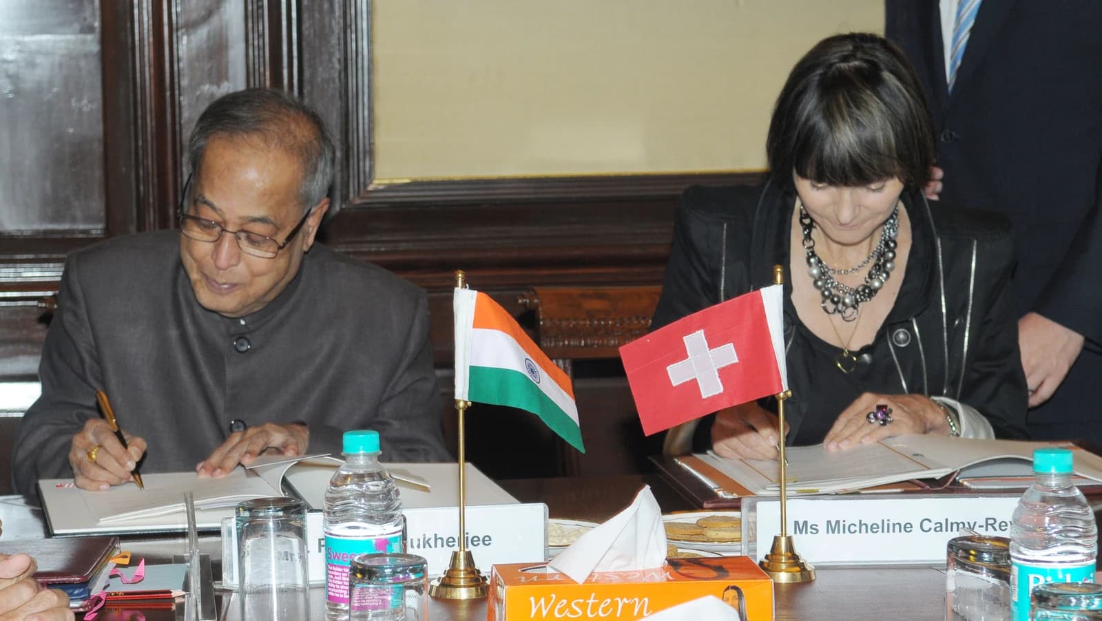 Pranab Mukherjee and Micheline Calmy Rey sign an agreement at a table.