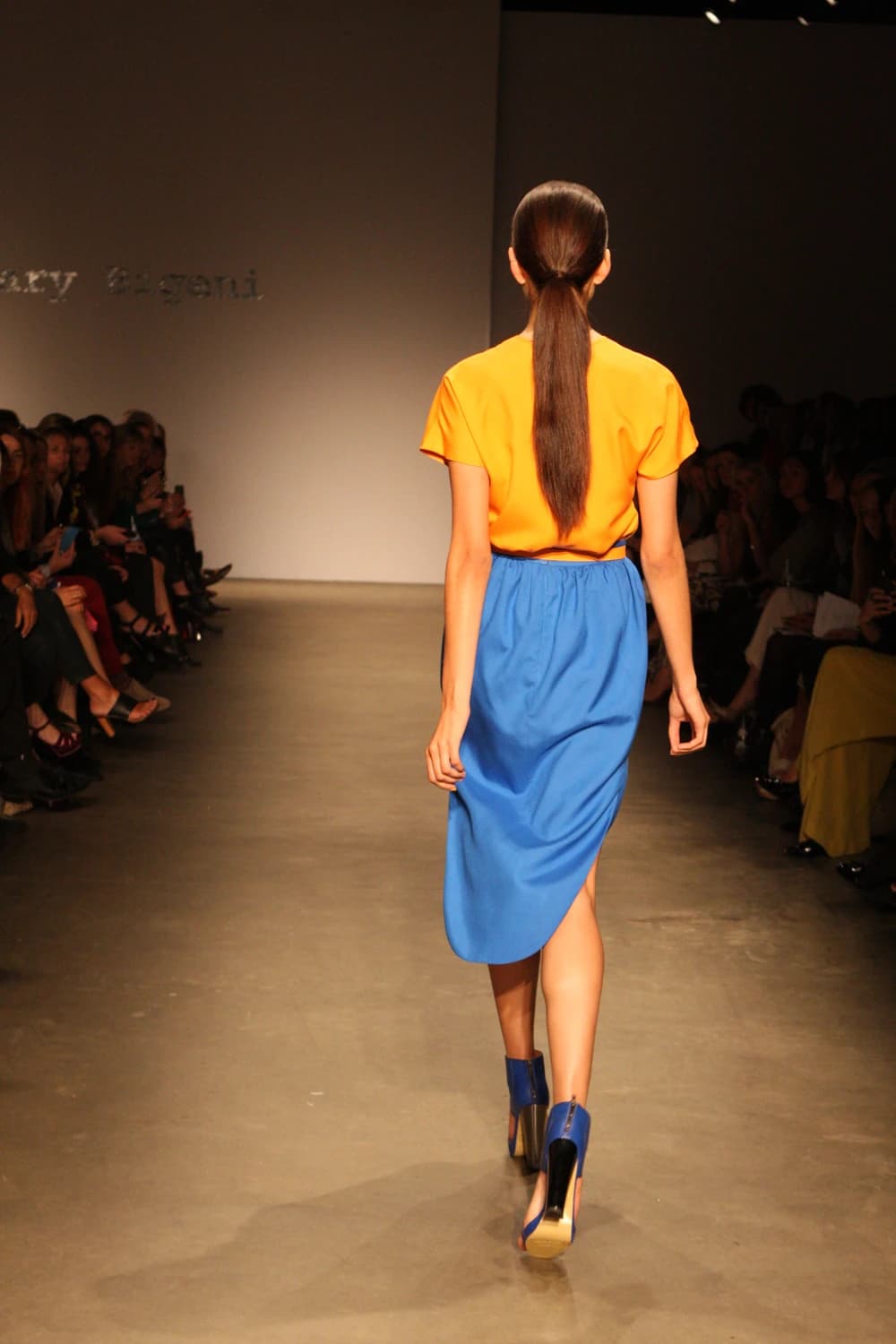 Model walks away from camera on runway, showcasing blue high-heeled shoes.