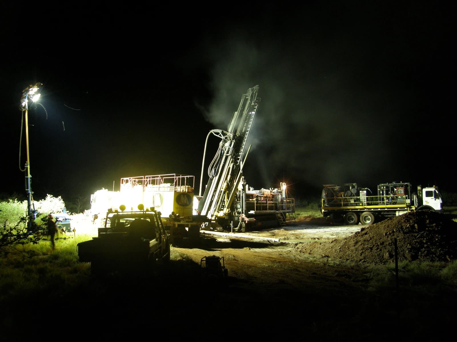 Reverse circulation drilling rig and support vehicles operating at a mine site at night.