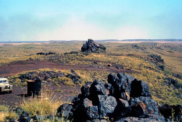 Arid landscape of Mount Goldsworthy Knob with scattered dark rocks and a small vehicle.