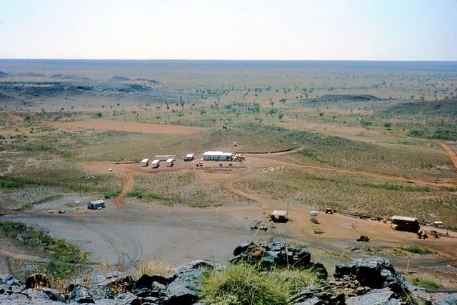 Aerial view shows exploration camp with scattered buildings in a vast, arid landscape.