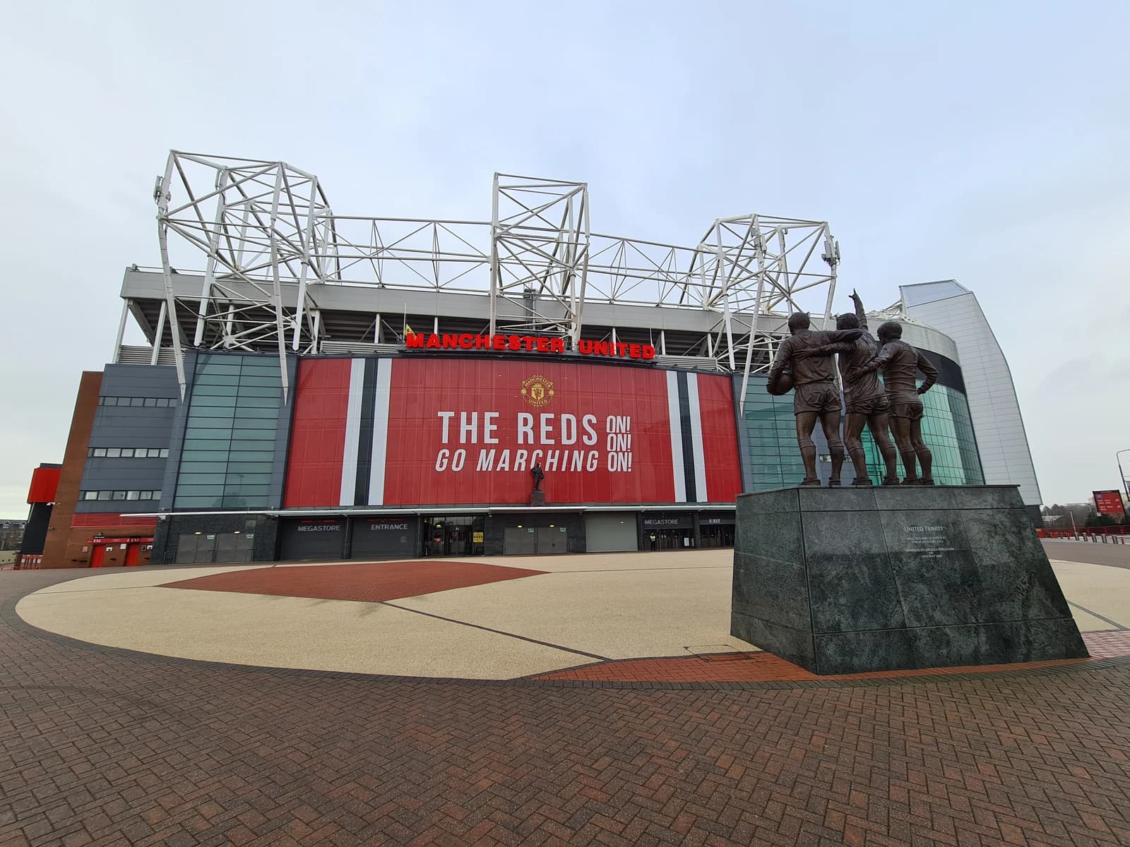 Exterior view of Old Trafford stadium and the 'United Trinity' statue.