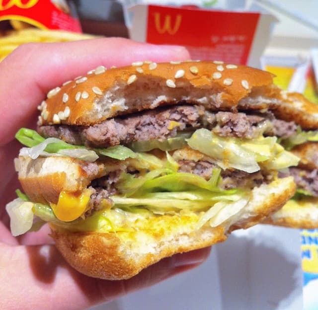 A person holds a partially eaten Big Mac hamburger with visible layers of patty, lettuce, and bun.