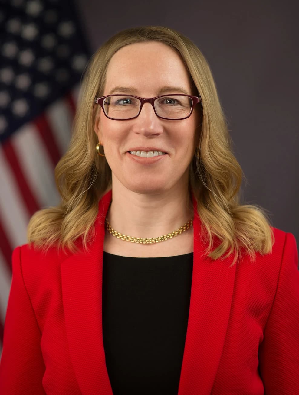Hester Peirce, SEC Commissioner, smiling in an official portrait with the American flag.