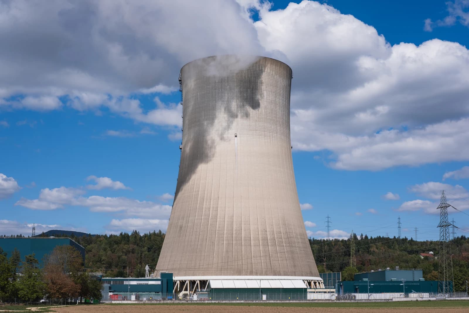Cooling tower of the Gösgen Nuclear Power Plant, releasing vapor against a blue sky.