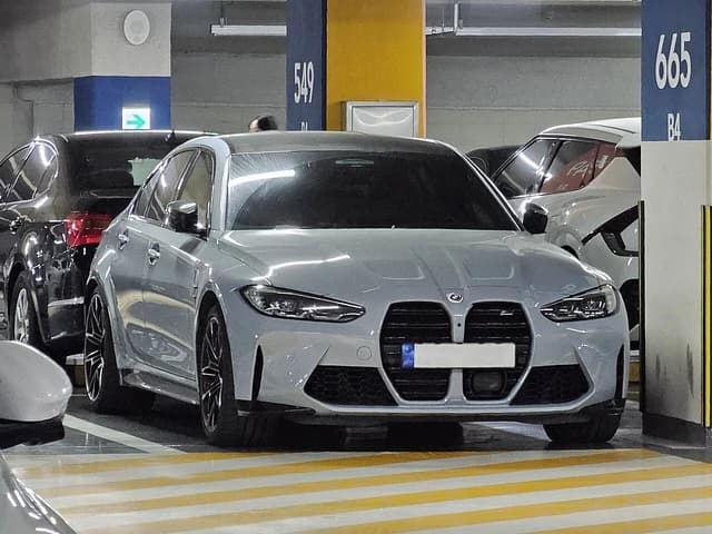 A grey BMW M3 Competition G80 parked in an underground parking garage.