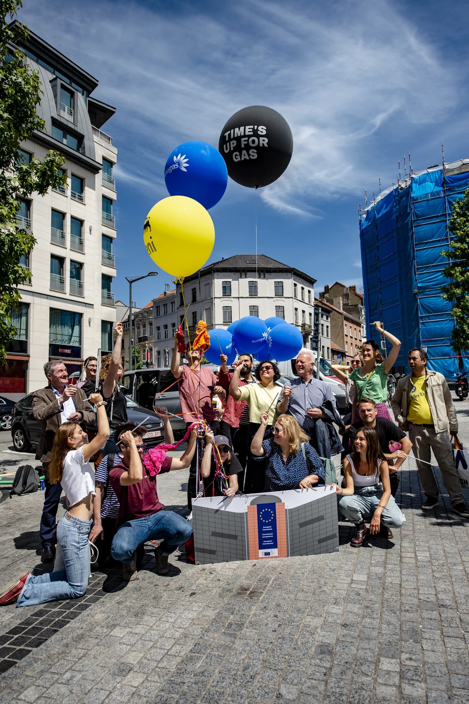 Group of activists in city street holding balloons and a model building.