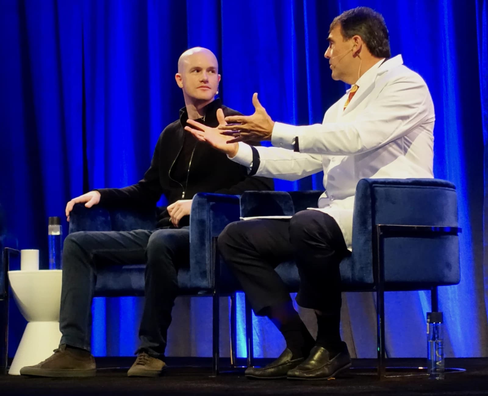 Brian Armstrong, CEO of Coinbase, seated on a stage next to another speaker.