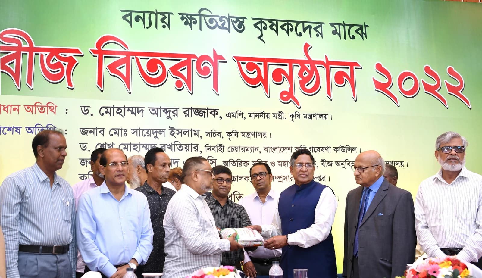 Agriculture Minister distributes seed packets to a farmer from a group of men.