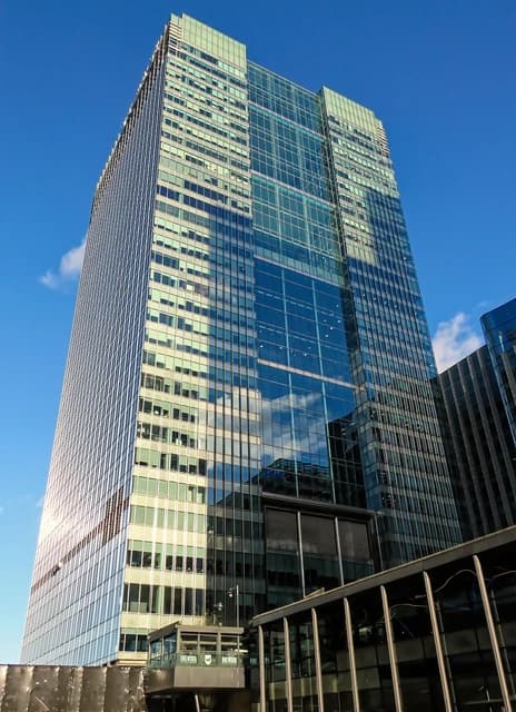 A modern glass skyscraper, 1 Churchill Place, against a clear blue sky.