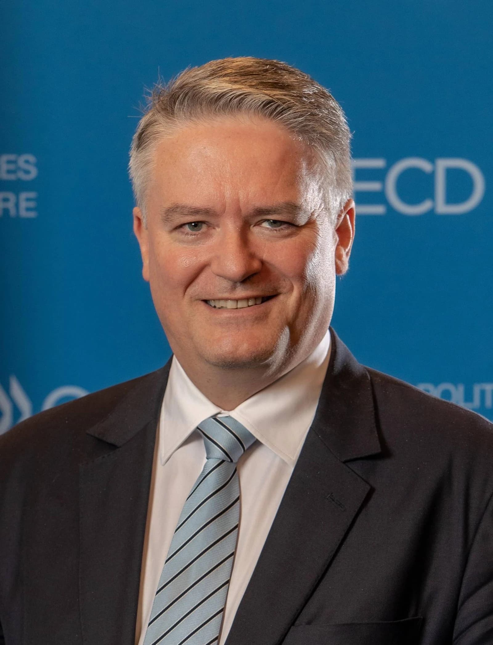 Mathias Cormann, OECD Secretary-General, smiling in a portrait against a blue background.