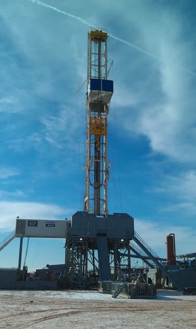Helmerich & Payne FlexRig drilling rig operating in an oil field under a bright blue sky.