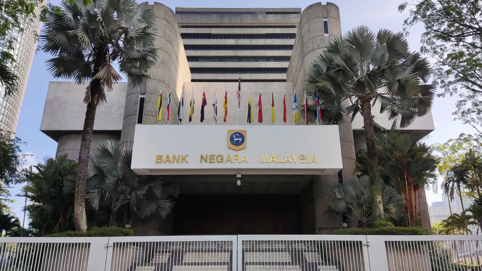 Exterior view of the Bank Negara Malaysia building with flags and palm trees.