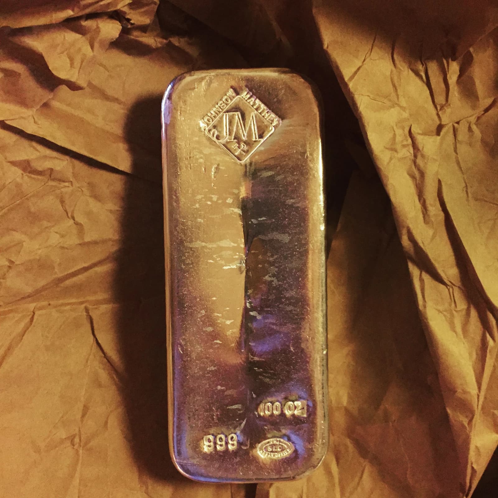 A rectangular 100 troy ounce silver bullion bar with 'Johnson Matthey' and '999' stamped on it.