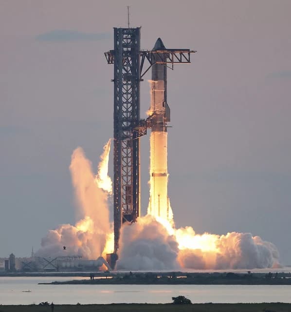 SpaceX Starship rocket igniting with large plumes of fire and smoke during a test flight.