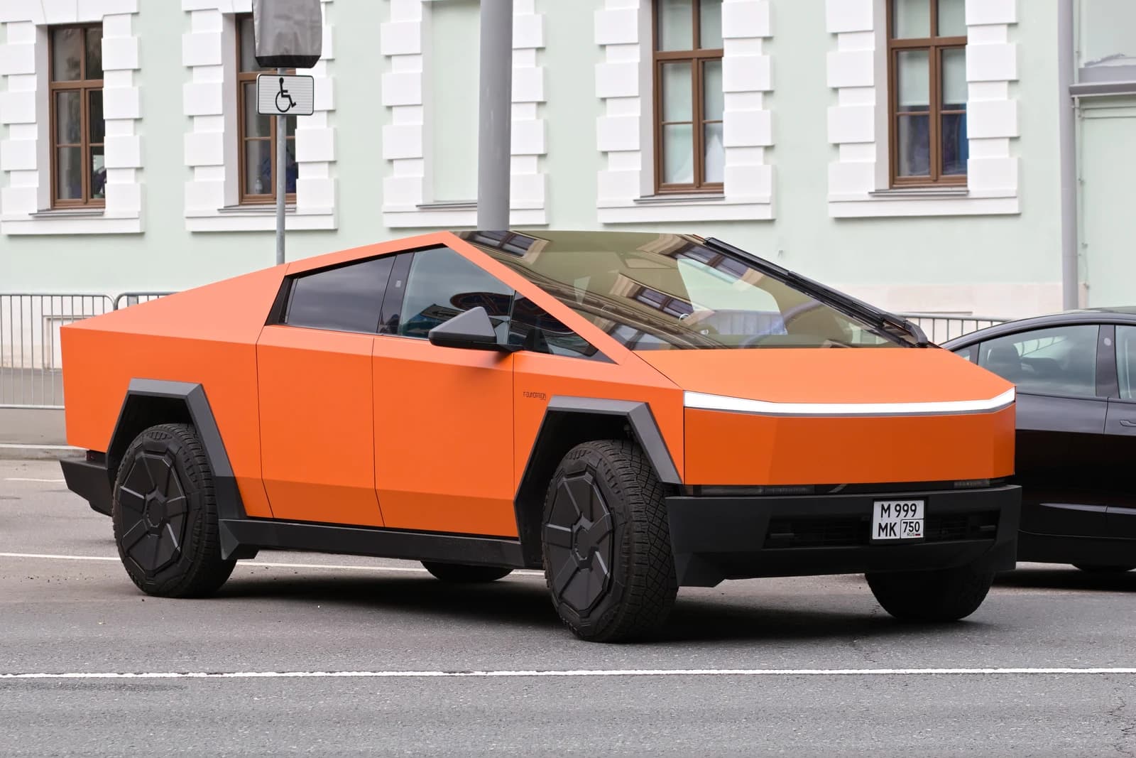 An orange Tesla Cybertruck is parked on a street in front of a building.