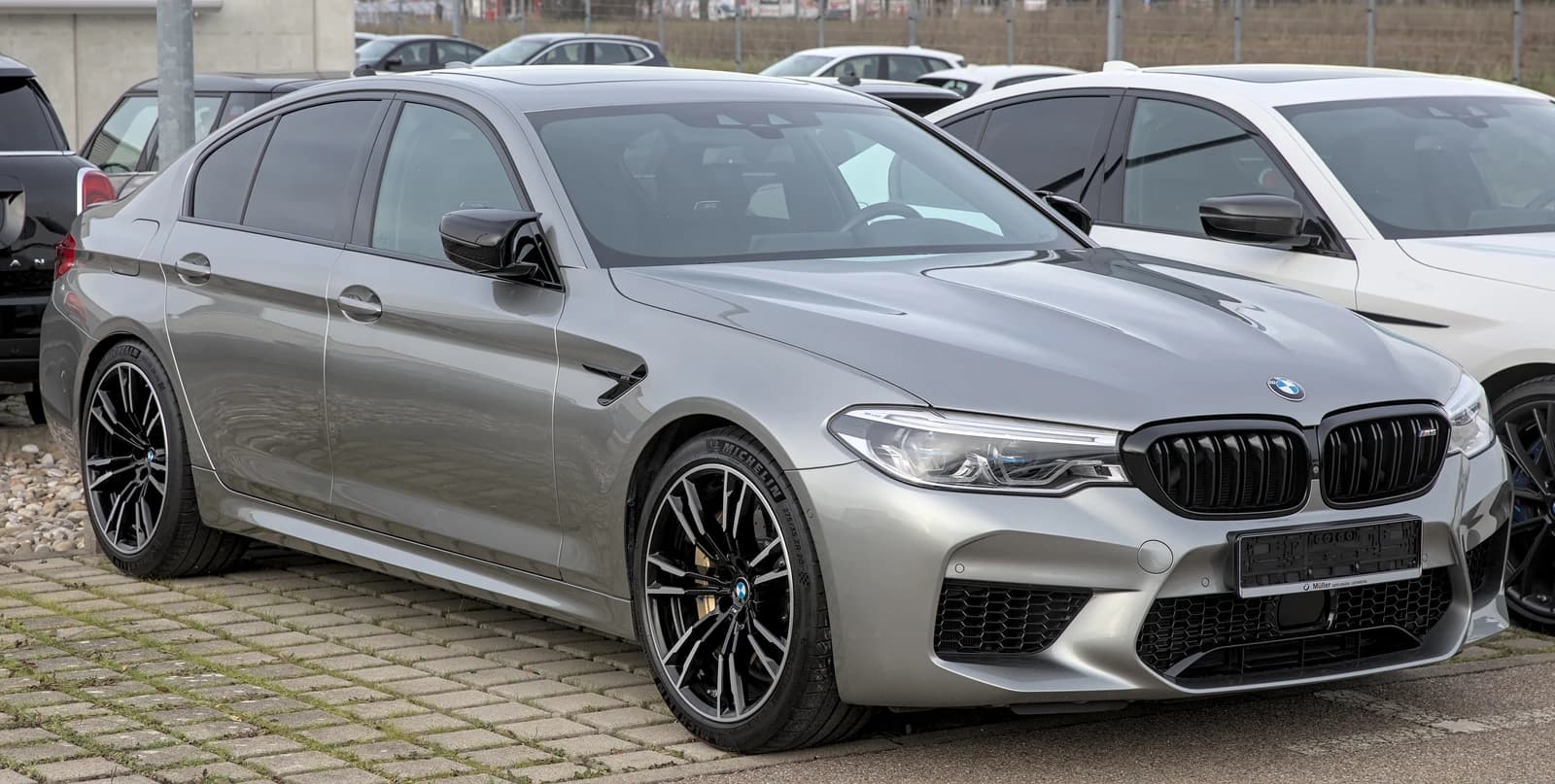 Gray BMW M5 F90 sedan parked on a paved lot outdoors.