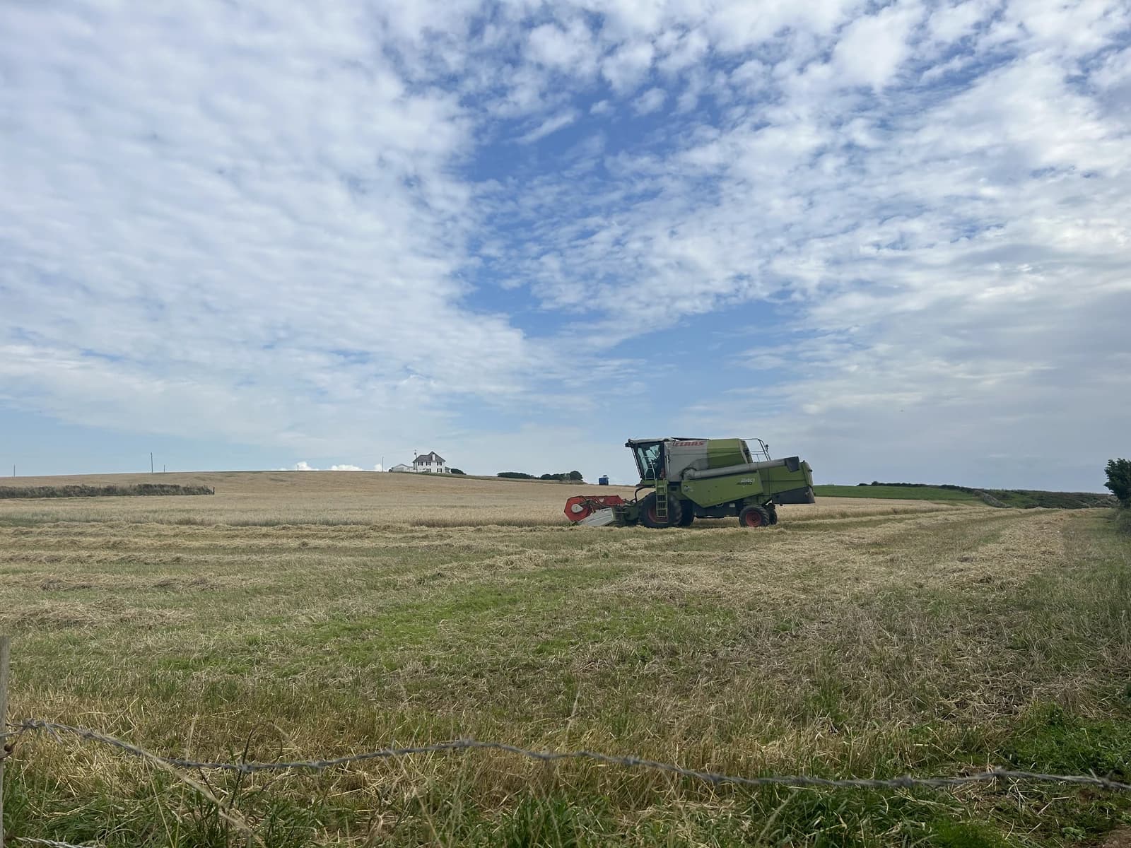 A combine harvester operates in a harvested wheat field near Rhossili, Gower, Wales.