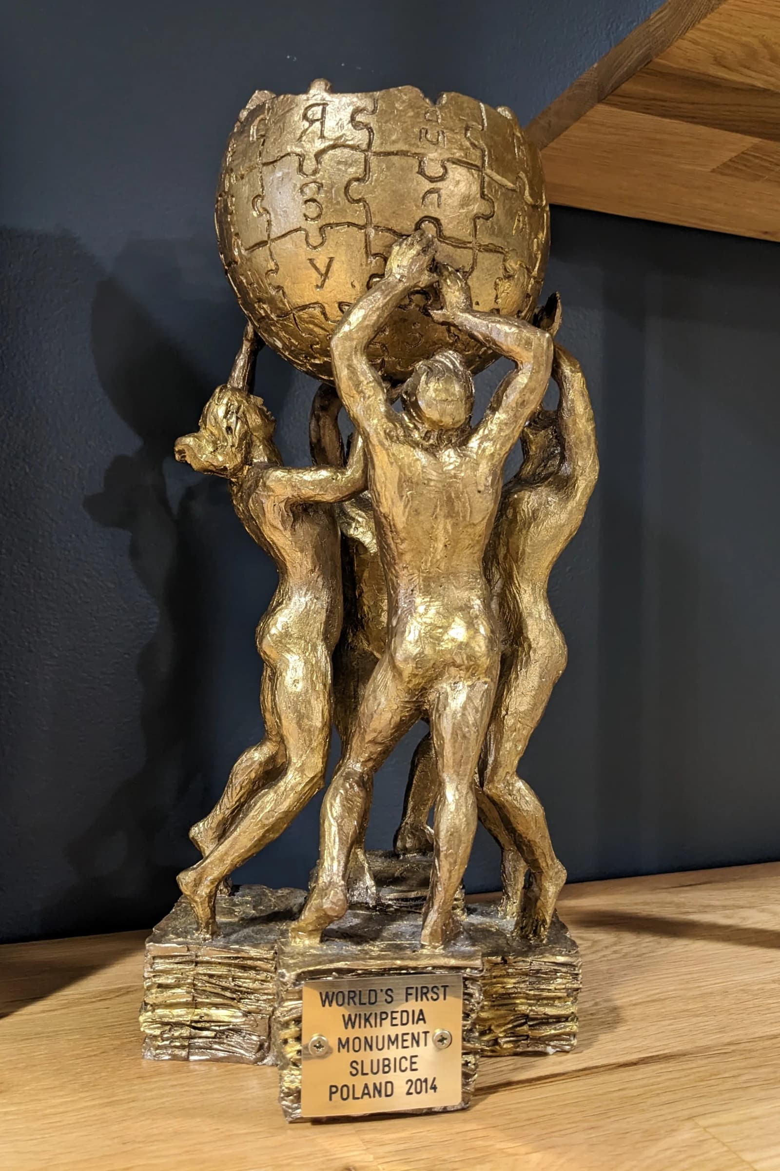 Golden Wikipedia Monument model, showing figures holding up a globe made of puzzle pieces.