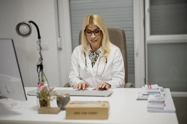 Female doctor in a white coat with a stethoscope using a computer and typing.