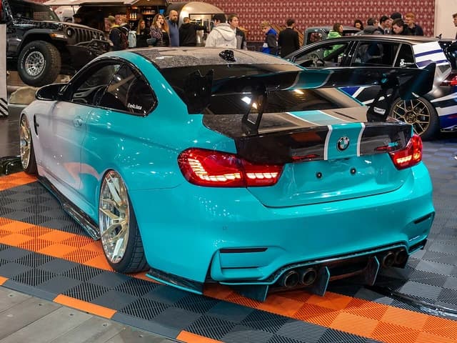 Modified teal BMW M4 with large rear spoiler and custom wheels.