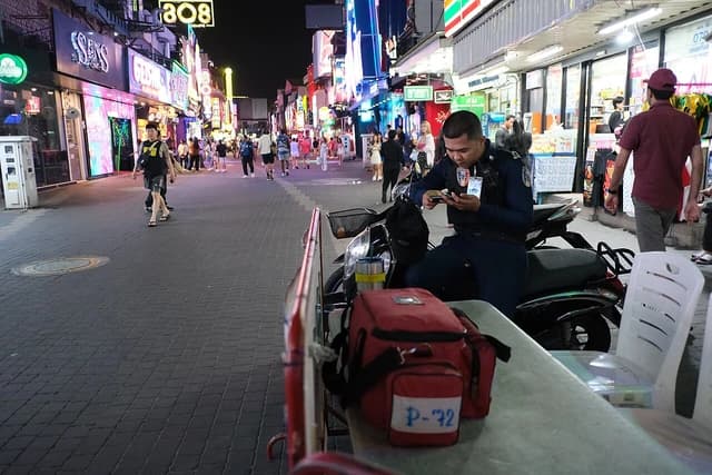 A person sits on a parked scooter checking their phone on a busy street.