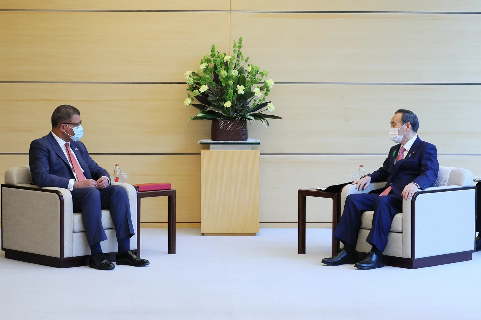 Yoshihide Suga and Alok Sharma, masked, sitting across from each other in a formal room.