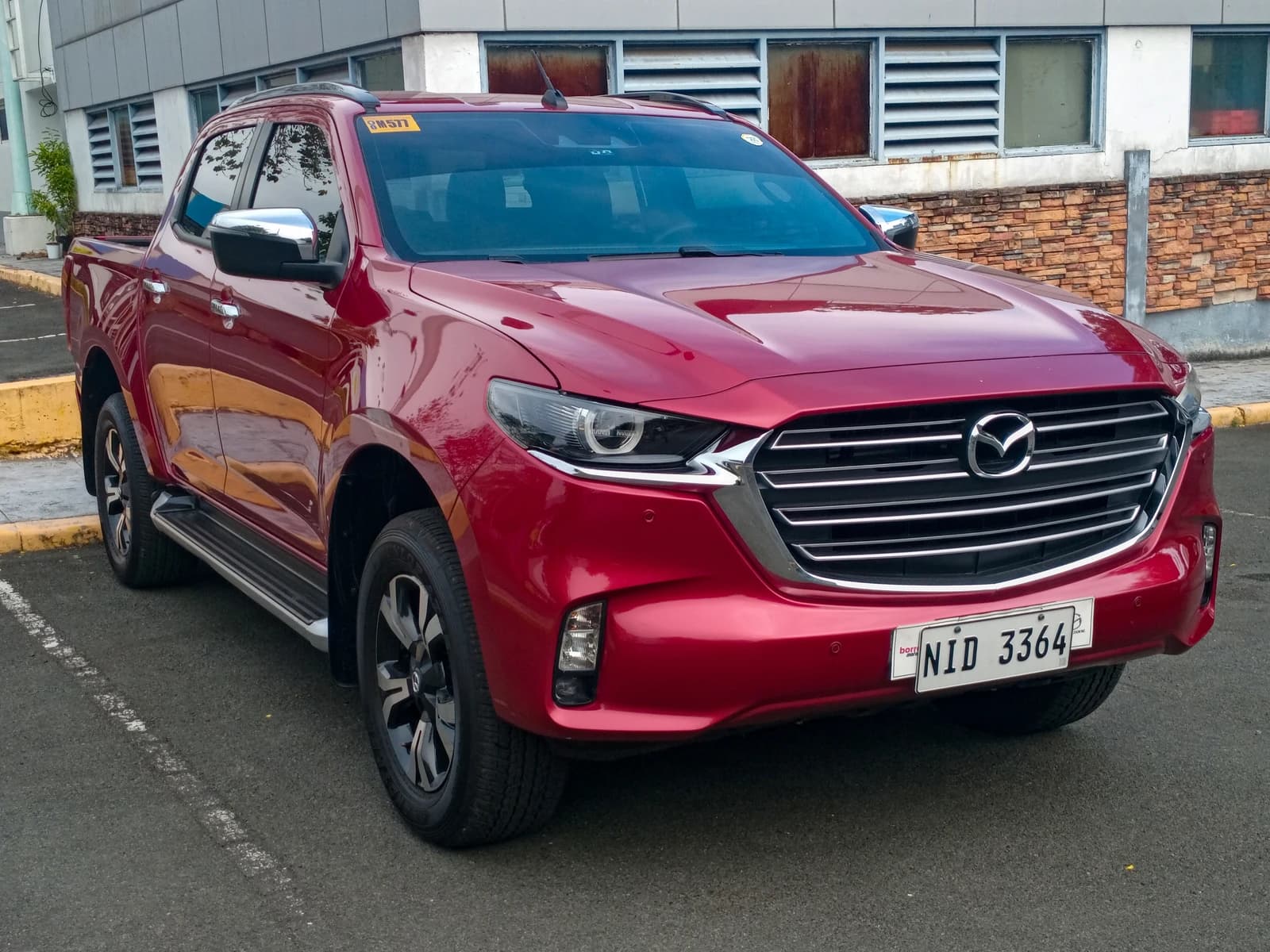 New generation red Mazda BT-50 4x4 pickup truck parked on asphalt near a building.
