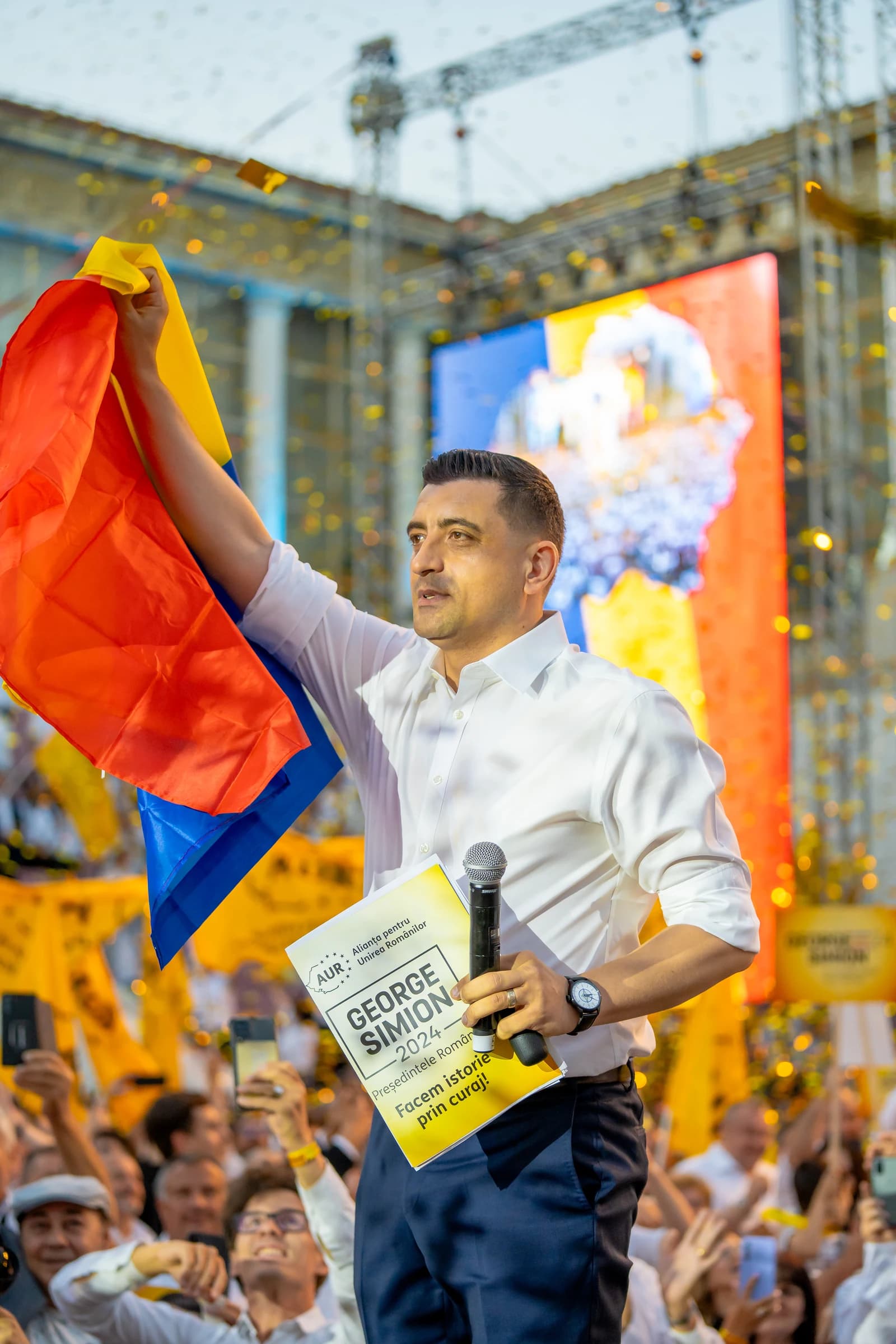 George Simion, leader of AUR, speaking at a rally with a Romanian flag.