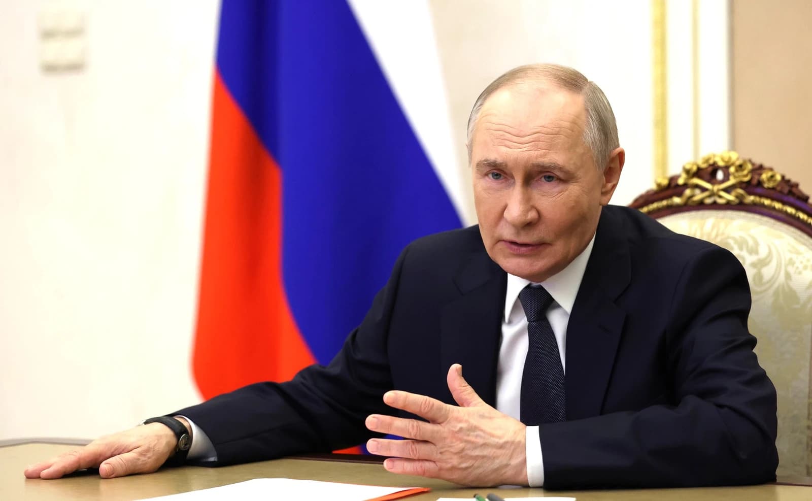 Russian President Vladimir Putin seated at a table, gesturing during a meeting.