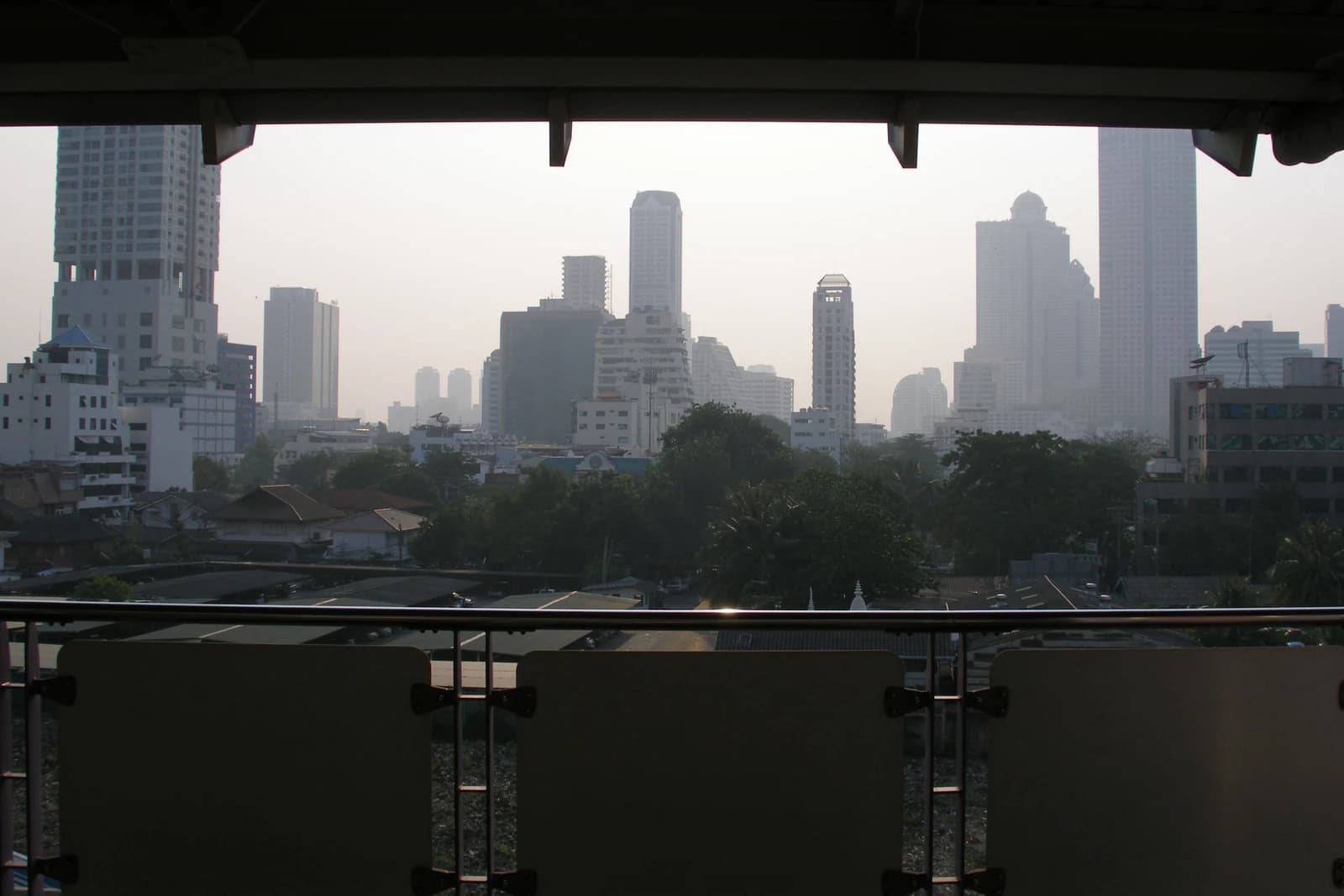 Skyscrapers and buildings in the hazy Bangkok skyline, viewed from an elevated platform.