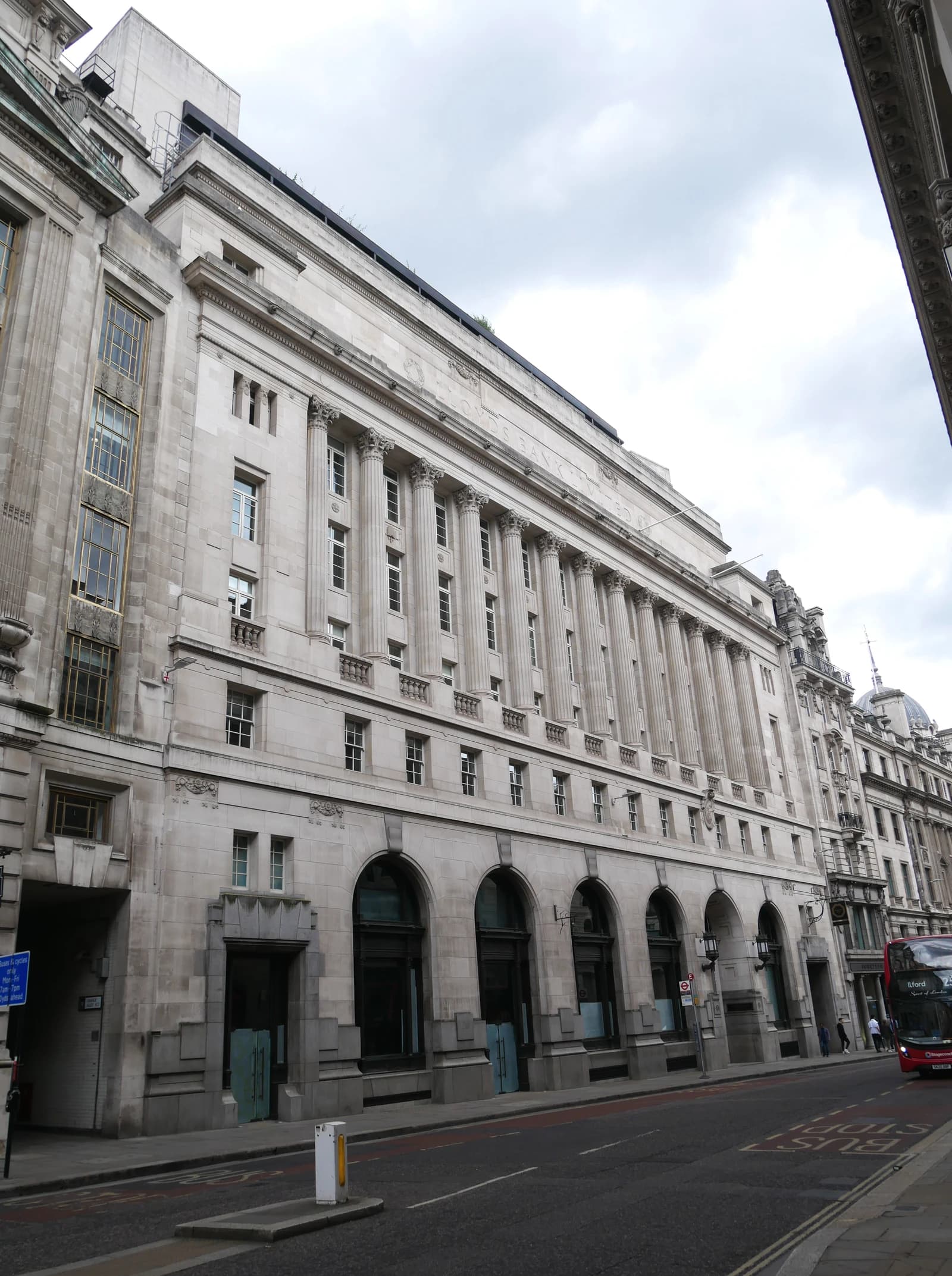 Exterior of a grand stone building with columns and arched windows on a city street.
