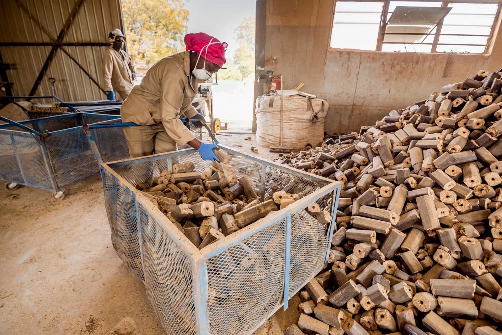 A worker sorts briquettes into a large metal cart inside a production facility.