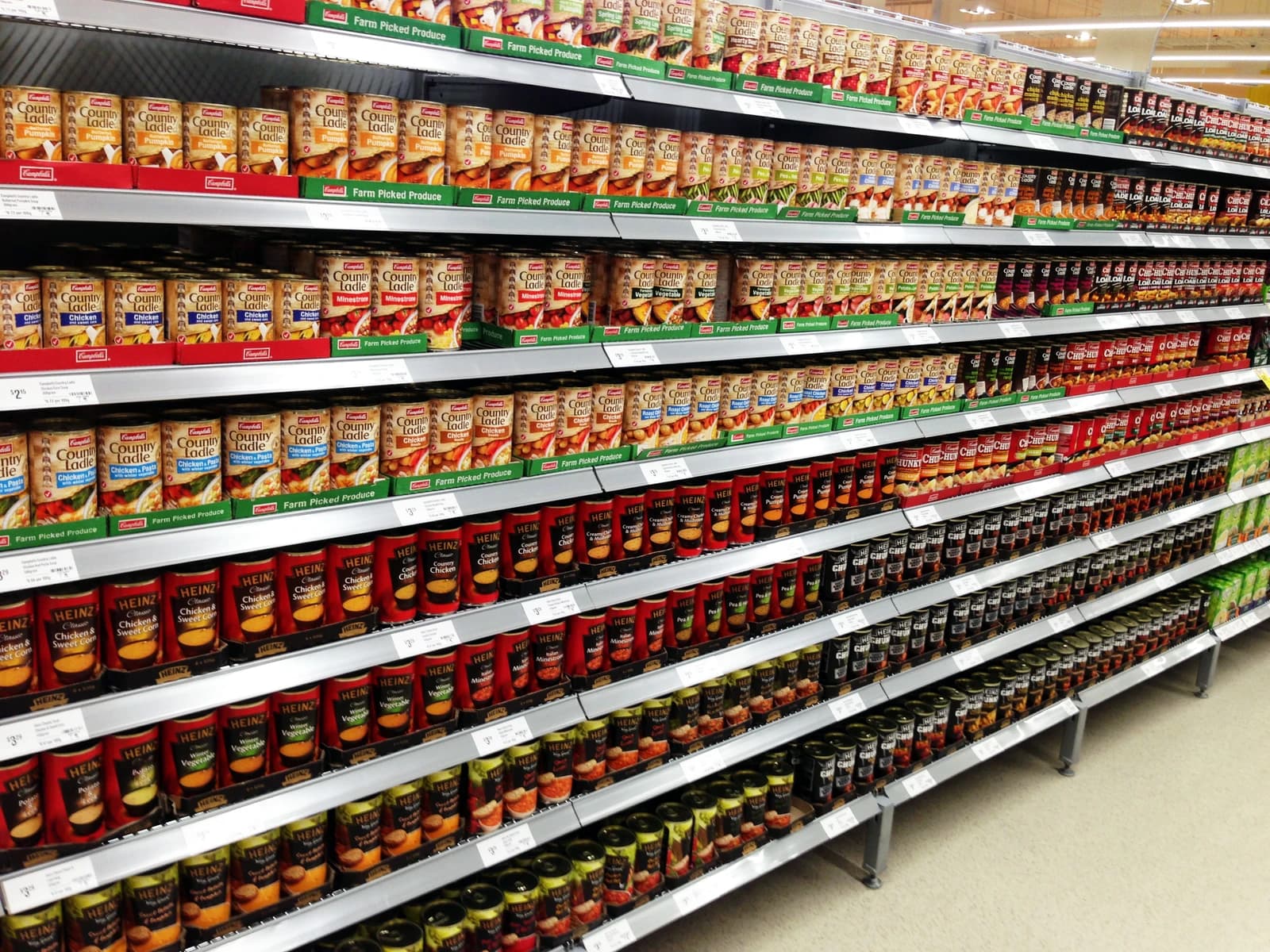 Supermarket aisle filled with multiple rows of various canned goods on display shelves.
