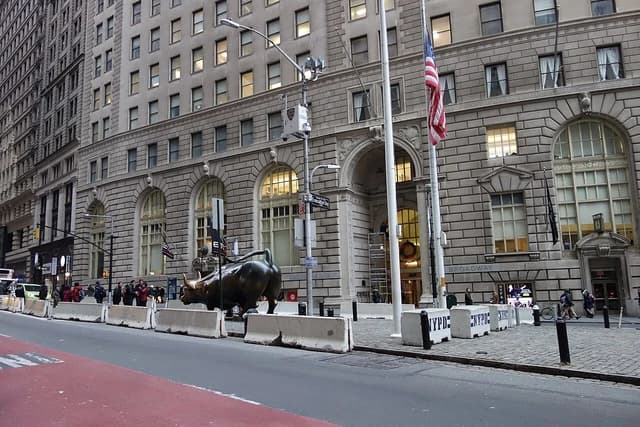 The Charging Bull sculpture stands on Broadway in Bowling Green, New York City, against a building facade.