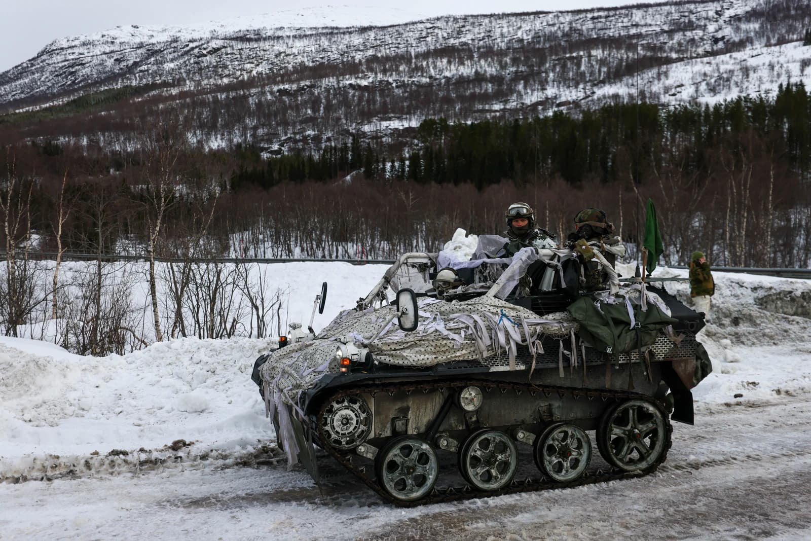 Military personnel on a tracked armored vehicle in a snowy, mountainous landscape.
