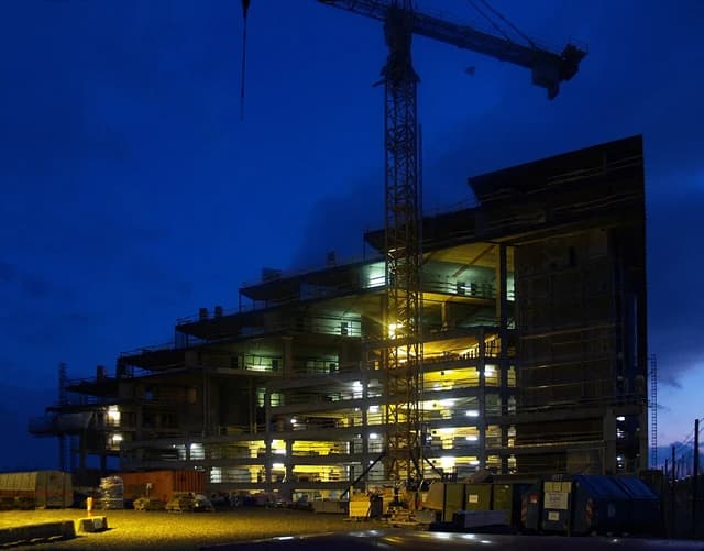 Construction site of a building designed by Bjarke Ingels Group, with crane visible at night.