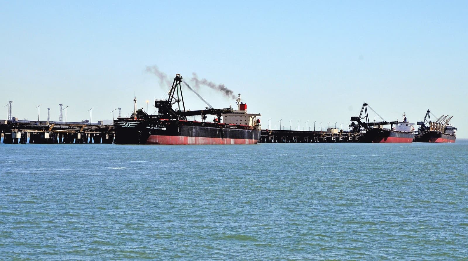 Two large bulk carrier ships are docked at the Port of Gladstone pier.
