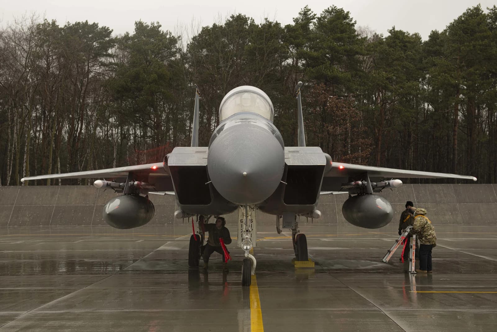 Ground crew preparing an F-15 fighter jet on a wet airfield in Poland.